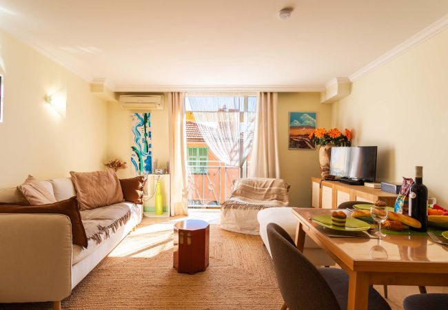 Bright living room with a comfy sofa, TV, dining table, and a window offering a view of the sunny outdoors.